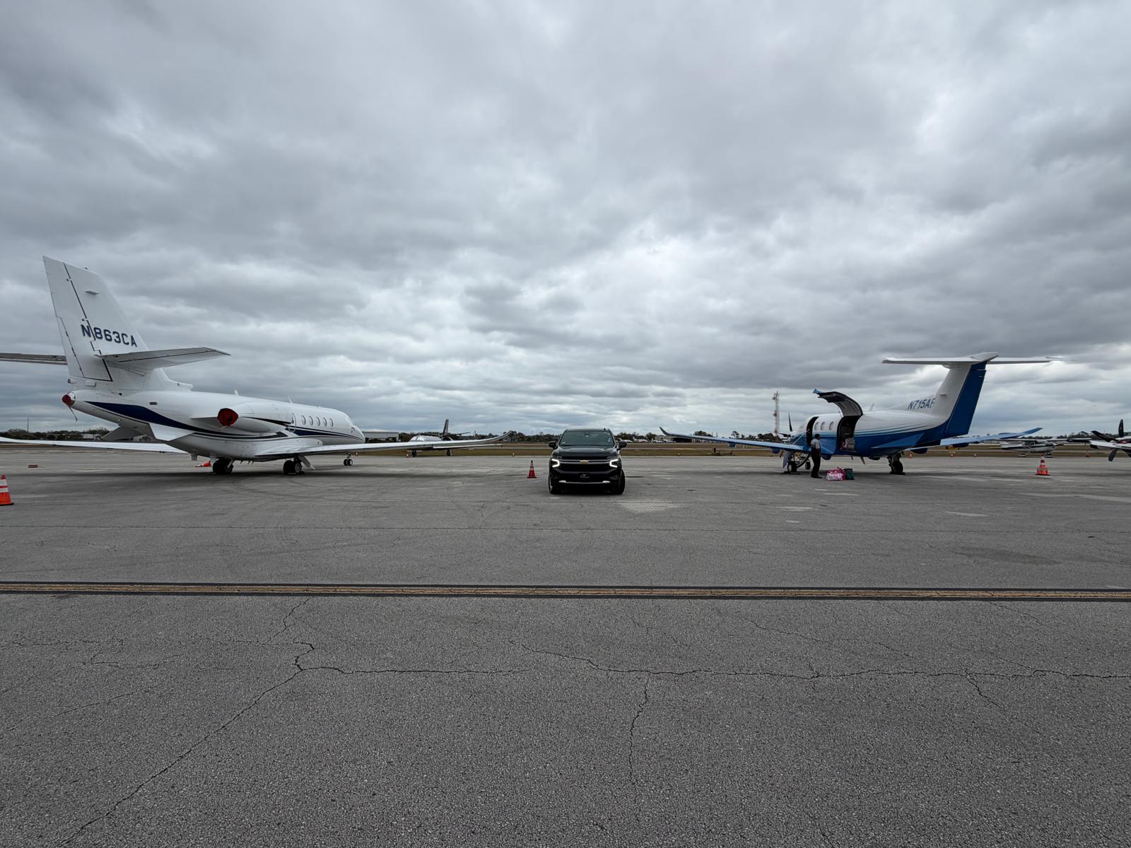 Black SUV parked on tarmac with multiple private jets, representing luxury airport limo service.